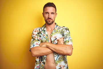 Handsome man wearing summer hawaiian flowers shirt over yellow isolated background skeptic and...