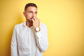 Young handsome man wearing elegant white shirt over yellow isolated background looking stressed and nervous with hands on mouth biting nails. Anxiety problem.