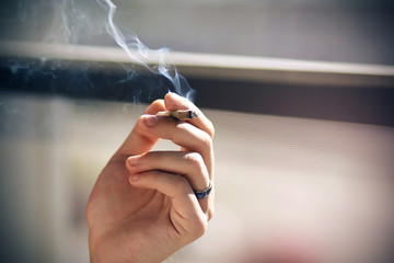 The hand of a man with a blue ring on his finger holds in his fingers a Smoking cigarette,...