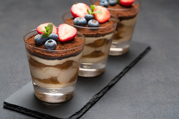 Classic tiramisu dessert with blueberries and strawberries in a glass on stone serving board on dark concrete background