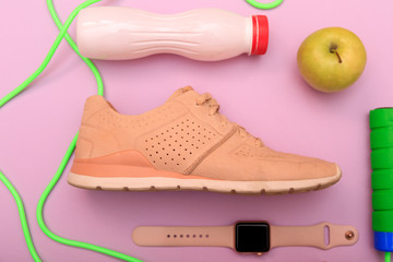 Fototapeta na wymiar Sport shoes, dumbbells and skipping rope on pink background. Top view. Set for sports activities and smart watch, apple and sneakers on pink background. Fitness and healthy life concept.