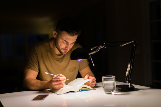 Young Handsome Man Studying At Home, Reading A Book At Night