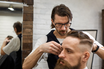Fototapeta premium Master cuts hair and beard of men in the barbershop, hairdresser makes hairstyle for a young man
