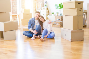 Fototapeta na wymiar Young beautiful couple relaxing sitting on the floor around cardboard boxes at home, smiling happy moving to a new house