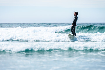 Surfer guy surfing with surfboard on waves in Atlantic ocean.