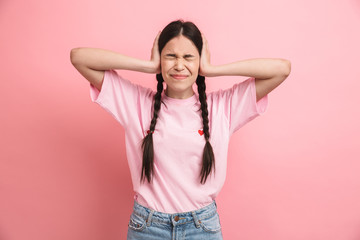 Image of puzzled teen girl with two braids standing at camera and covering her ears with hands