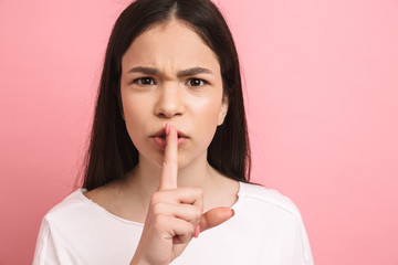 Naklejka premium Portrait closeup of frowning girl with long dark hair holding index finger on lips and asking to be quiet