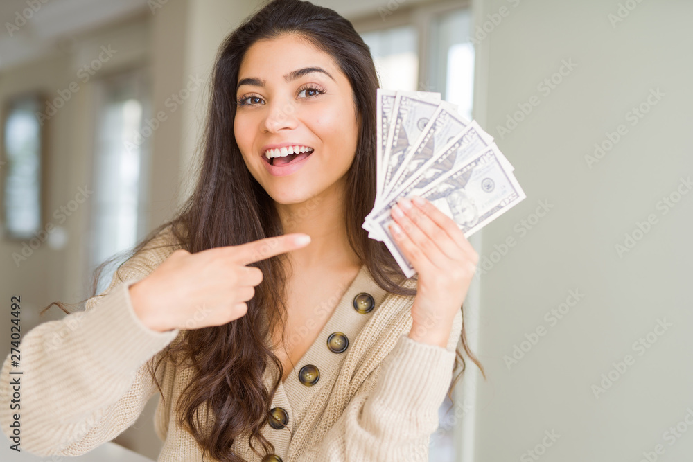 Wall mural young woman holding 50 dollars bank notes very happy pointing with hand and finger