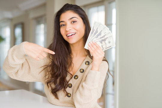 Young woman holding 20 dollars bank notes with surprise face pointing finger to himself