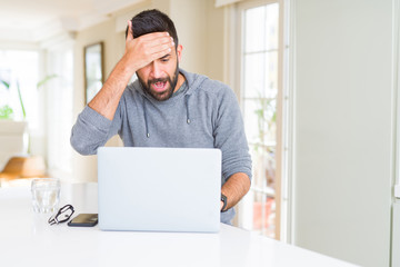 Handsome hispanic man working using computer laptop stressed with hand on head, shocked with shame and surprise face, angry and frustrated. Fear and upset for mistake.