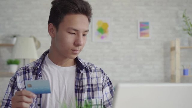 young asian man in a shirt enters data with a Bank card on a laptop close up