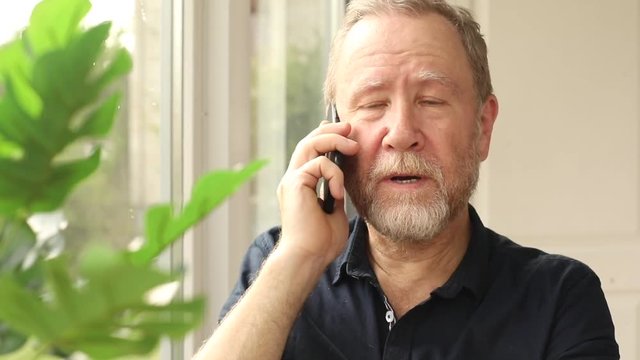 front view of elderly bearded man talking on smartphone indoors calm serious face expression business people modern lifestyle technology digital device communication online website 3G 4G free wifi