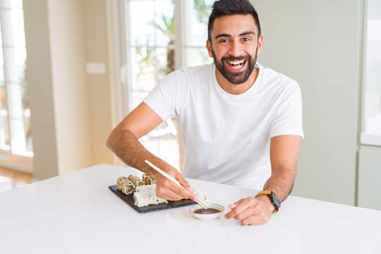 Handsome man smiling happy enjoying eating fresh colorful asian sushi using chopsticks