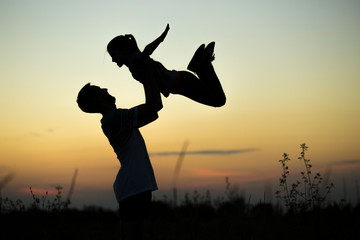 Silhouette of father throwing up his happy daughter in the air at sunset. family time togehter