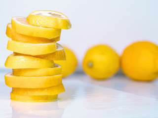 Obraz na płótnie Canvas Set of whole yellow lemon and pile of slices on light table. Lemon slices piled together on table. Fruits composition. Blurred background. Selective soft focus