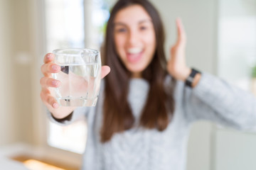 Beautiful young woman drinking a fresh glass of water very happy and excited, winner expression celebrating victory screaming with big smile and raised hands