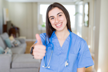 Beautiful young nurse woman wearing uniform and stethoscope at the clinic doing happy thumbs up gesture with hand. Approving expression looking at the camera with showing success.