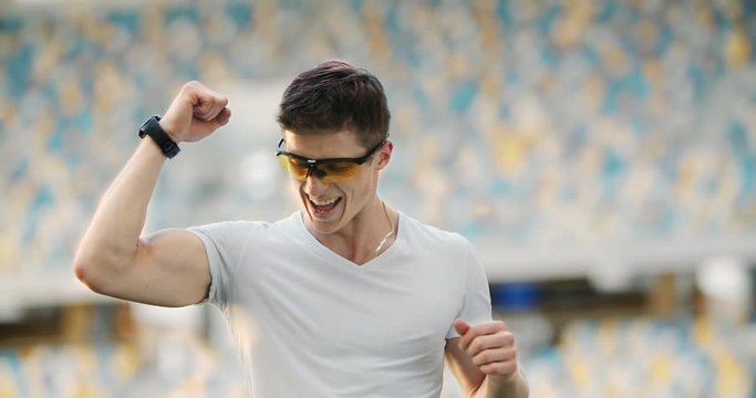 Smiling successful male athlete checking data on smartwatch and making yes gesture, beating personal record.