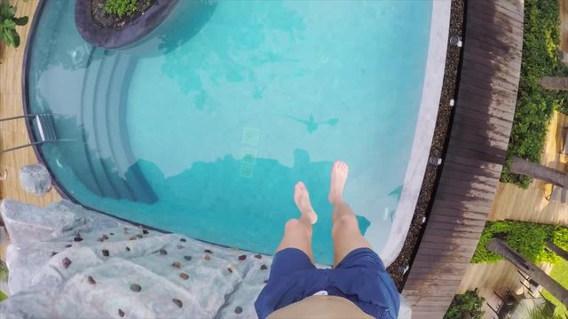 Slow motion go pro view of man's feet jumping into swimming pool from climbing wall