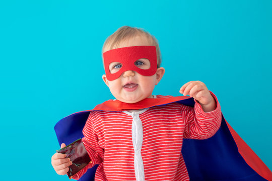 Back view of cute baby in superhero mask and cape looking at camera blue background