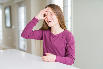 Fototapeta premium Beautiful young girl kid on white table doing ok gesture with hand smiling, eye looking through fingers with happy face.