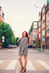 Red-haired Model in a coat posing against the backdrop of the sunset on the street.