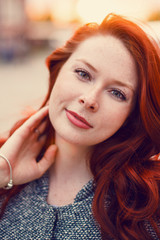 Fototapeta premium Red-haired Model in a coat posing against the backdrop of the sunset on the street.