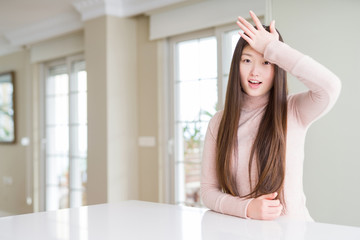 Beautiful Asian woman wearing casual sweater on white table surprised with hand on head for...