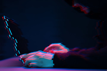 Hacker in the hood working with laptop typing text in dark room. Image with glitch effect