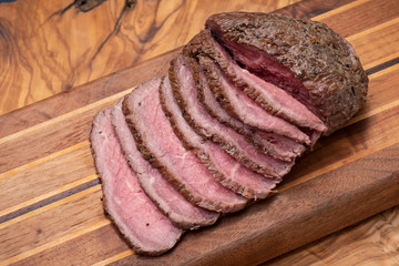 Sliced Grass Fed juicy Corn Roast Beef on natural wood cutting board.