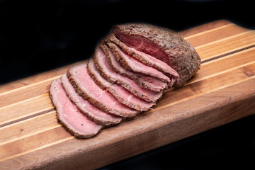 Sliced Grass Fed juicy Corn Roast Beef on natural wood cutting board.