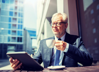 business, technology and people concept - senior businessman with tablet pc computer drinking coffee at city street cafe