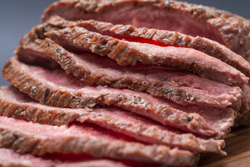 Sliced Grass Fed juicy Corn Roast Beef on natural wood cutting board.