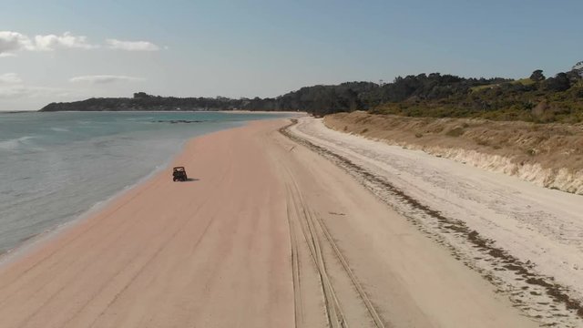 Aerial drone follow tracking shot of a dune buggy speeding on the sandy beach near the water