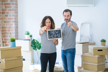 Middle age senior couple holding blackboard moving to a new home pointing with finger to the camera and to you, hand sign, positive and confident gesture from the front