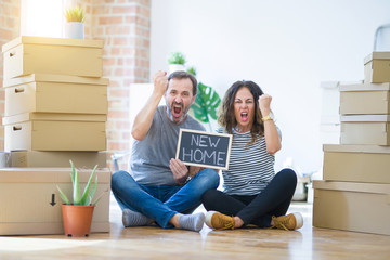 Middle age senior couple sitting on the floor holding blackboard moving to a new home annoyed and frustrated shouting with anger, crazy and yelling with raised hand, anger concept