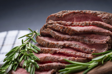 Sliced Grass Fed juicy Corn Roast Beef garnished with Rosemary Fresh Herb on natural wood cutting board.