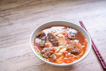 Beef noodle ramen meal with tomato sauce broth in bowl on bright wooden table, famous chinese style food in Taiwan, close up, top view, copy space