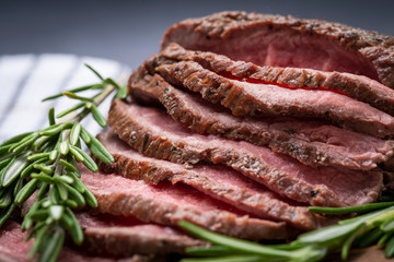 Sliced Grass Fed juicy Corn Roast Beef garnished with Rosemary Fresh Herb on natural wood cutting board.