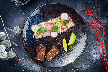 Top view on sea bass ceviche served in dark plate on black stone background. Top view food. Flat lay seafood. Fresh and tasty cebiche. Raw fish. Latin America cuisine. Lunch