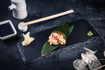 Close-up of tasty hand roll sushi with scallop and Tobico caviar served on dark stone plate with soy sauce and ginger. Copy space. Temaki, Japanese cuisine. Healthy food