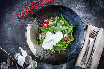 Sorrel salad with tomatoes and sour cream.Top view. Flat lay food. Fresh, green, vegan salad for lunch. Salad in black bowl on dark background view from above.