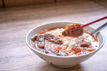 Beef noodle ramen meal with tomato sauce broth in bowl on bright wooden table, famous chinese style food in Taiwan, close up, top view, copy space