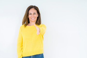 Beautiful middle age woman wearing yellow sweater over isolated background smiling friendly offering handshake as greeting and welcoming. Successful business.