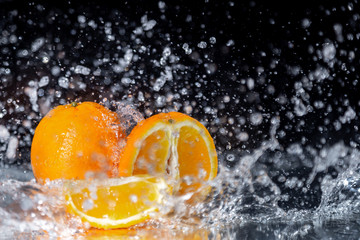 Fototapeta na wymiar Orange with water splash on black background with streaming water on it.