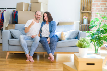 Fototapeta na wymiar Young couple sitting on the sofa arround cardboard boxes moving to a new house showing and pointing up with finger number one while smiling confident and happy.