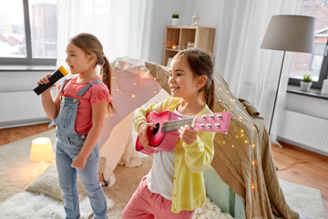 childhood, hygge and friendship concept - happy girls with guitar and microphone playing music and...