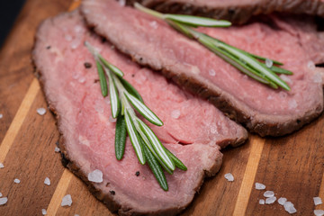 Sliced Grass Fed juicy Corn Roast Beef garnished with Rosemary Fresh Herb on natural wood cutting board.