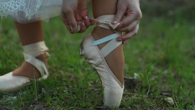Ballerina shoes during untying and tying shoes hands on grass outdoors during spring day closeup view captured in 120 fps