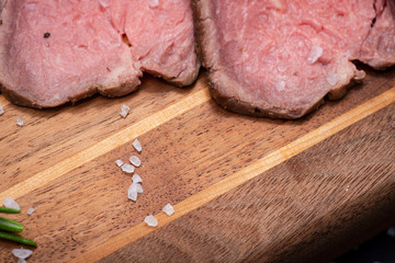 Sliced Grass Fed juicy Corn Roast Beef garnished with Rosemary Fresh Herb on natural wood cutting board.